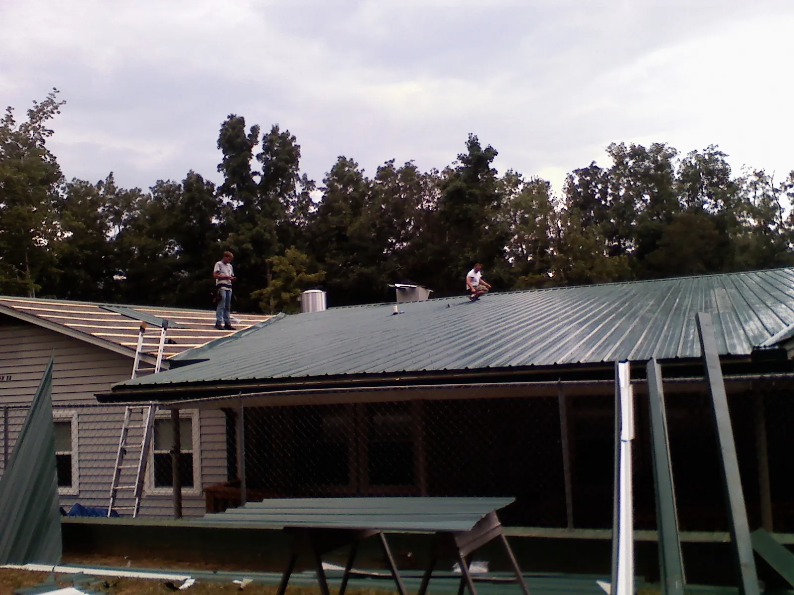 Two roofers installing green metal panels above a covered porch in Lewistown