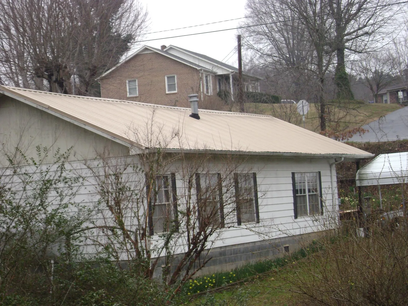 Tan metal roof on a white sided house set into a hillside — Commercial Roofing by Roofing Brothers in Lewistown